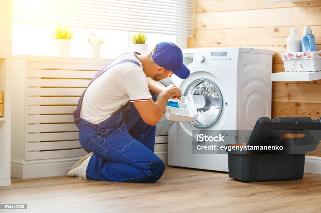 working man   plumber repairs  washing machine in   laundry working man plumber repairs a washing machine in   laundry Appliance Stock Photo