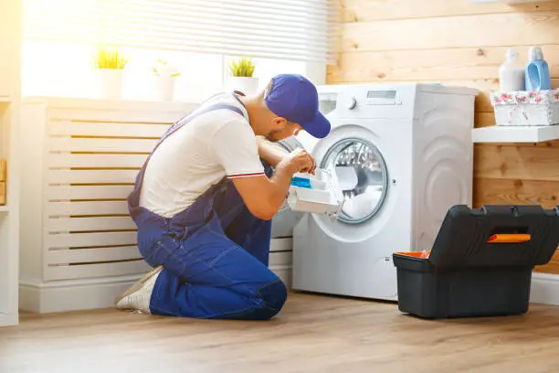 Photo of working man   plumber repairs  washing machine in   laundry