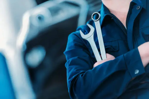 Closeup shot of an automechanic in overalls holding wrench and ring spanner