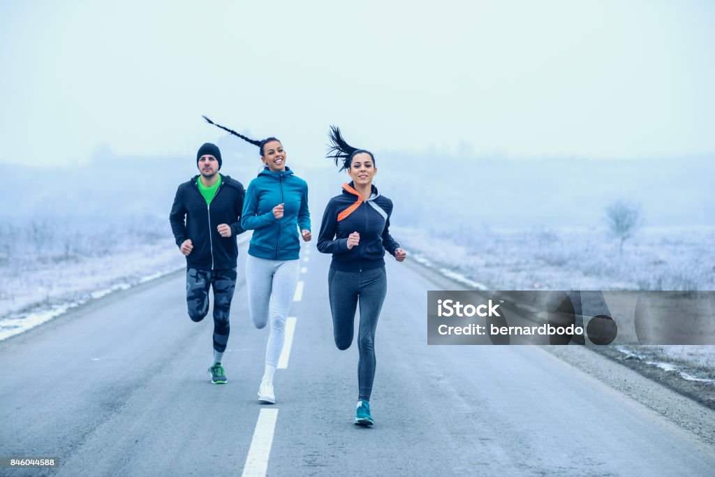 Defeating the road Athlete fitness friends running on an open road. Winter Stock Photo