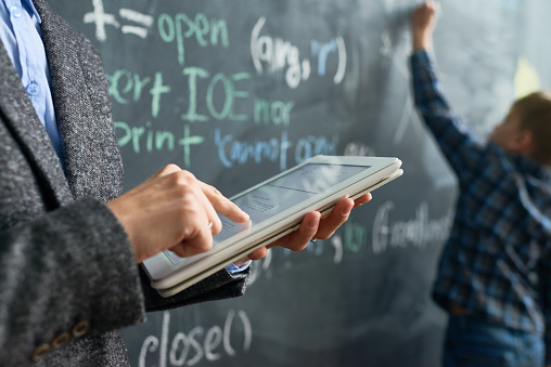 Close-up of unrecognizable female teacher using digital tablet while examining pupil at blackboard