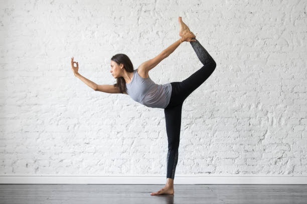 Young attractive woman in Natarajasana pose, studio background Young attractive woman practicing yoga, stretching in Natarajasana exercise, Lord of the Dance pose, working out, wearing sportswear, gray tank top, black pants, indoor full length, studio background Hot Yoga stock pictures, royalty-free photos & images