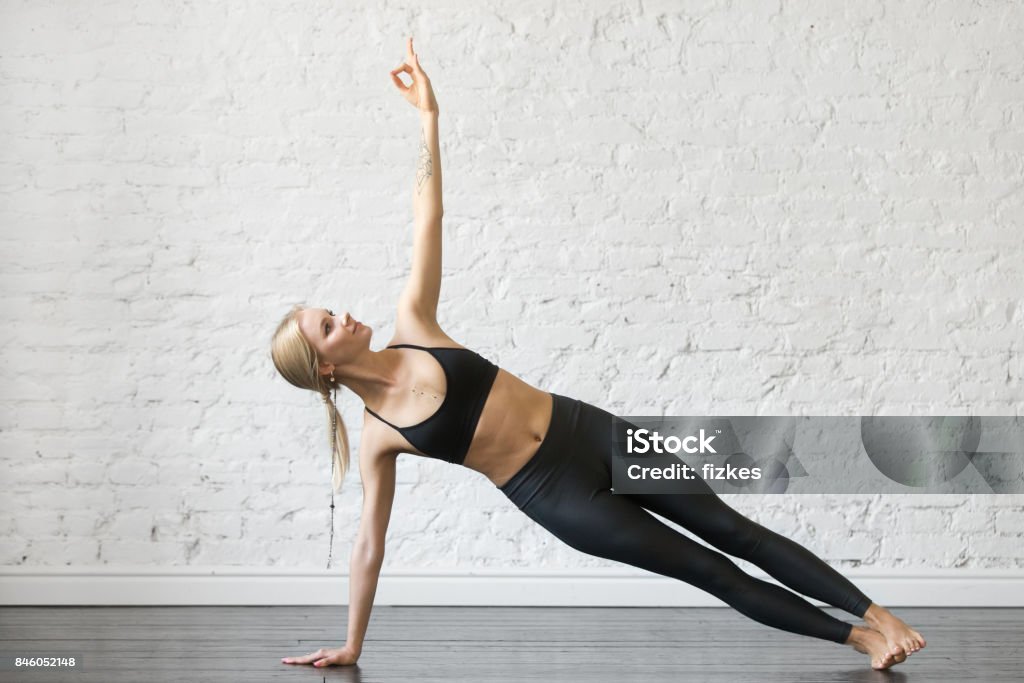Young attractive woman in Side Plank pose, studio background Young attractive woman practicing yoga, standing in Side Plank exercise, Vasisthasana pose, working out, wearing sportswear, black top and pants, indoor full length, studio background Side Plank Pose Stock Photo