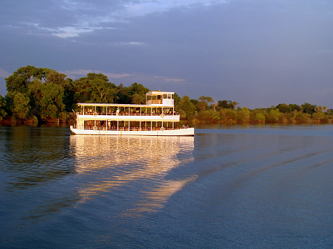 It is sunset time and a boat with tourists on board make a trip over the zambezi river on this romantic evening.