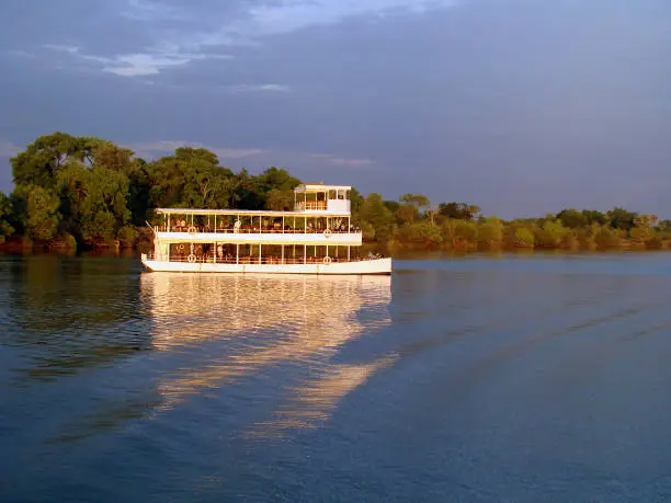 It is sunset time and a boat with tourists on board make a trip over the zambezi river on this romantic evening.