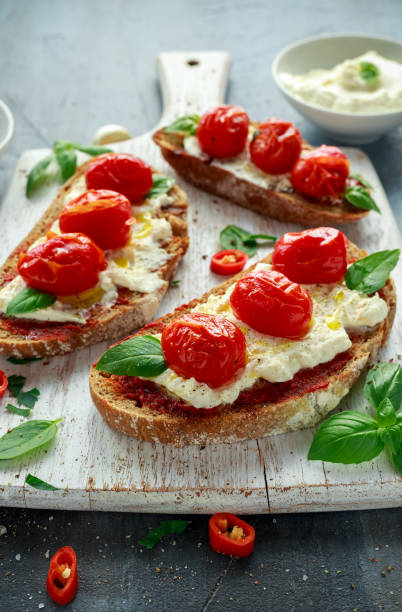 istock Tomato Ricotta Bruschetta with sun dried tomatoes paste, olive oil brown bread and basil in a white wooden board. 846062062