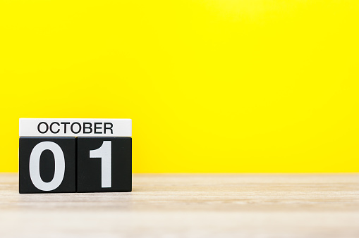 October 1st. Day 1 of month, wooden color calendar on yellow background. Autumn time. Empty space for text.
