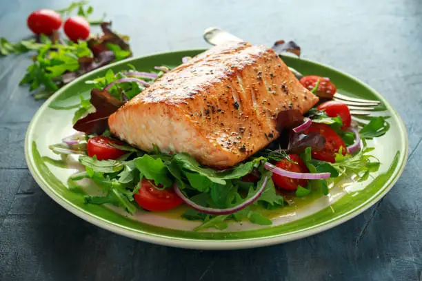 Baked salmon steak with tomato, onion, mix of green leaves salad in a plate. healthy food.