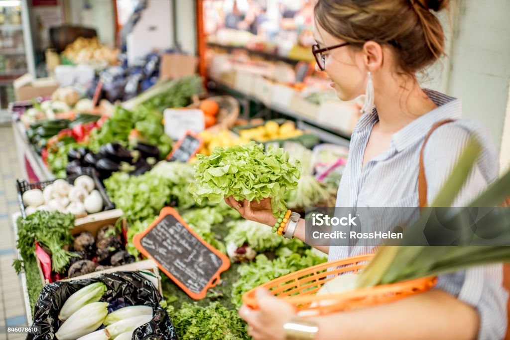 Woman at the food market Young woman choosing a fresh salad standing with basket at the food market in France Market - Retail Space Stock Photo