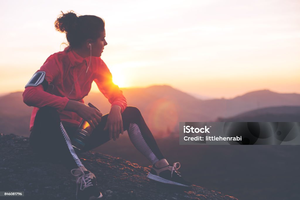 Fit woman athlete resting outdoors Athletic woman resting after a hard training in the mountains at sunset. Sport tight clothes. Running Stock Photo