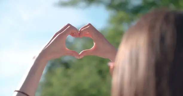 Photo of Female hands in shape of heart over green nature and blue sky.