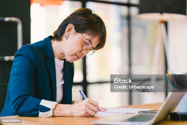 Beautiful Middle Age Asian Woman Working On Paperwork In Modern Contemporary Office With Laptop Computer Business Owner Entrepreneur Executive Manager Or Employee Office Worker Concept Stock Photo - Download Image Now