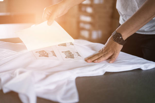 giovane donna estrarre la carta dalla pellicola impermeabile sul tessuto in negozio. lavoratore che lavora sulla serigrafia manuale su t-shirt. - textile print foto e immagini stock