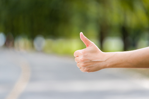 Close up woman hand hitchhiking at countryside road near forest,Alone travel or single traveller or hitchhiker concept.