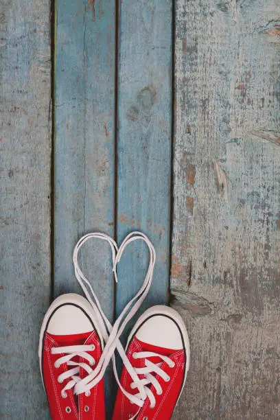 Photo of A pair of red retro sneakers on a blue wooden background, laces lined in a heart shape. Concept of young hipster love