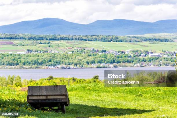 Old Vintage Wooden Wagon Overlooking Saint Lawrence River In Summer Landscape Field In Countryside With Small Village Houses Stock Photo - Download Image Now