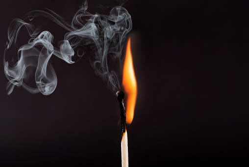 Matches stick with the flame and smoke burning, isolated on a black background, close up