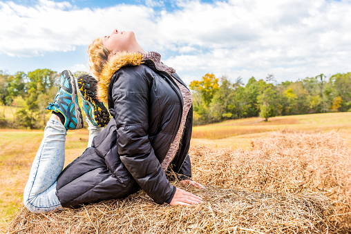 Young woman in downward arch backbend yoga pose on hay roll bale in autumn countryside at farm field
