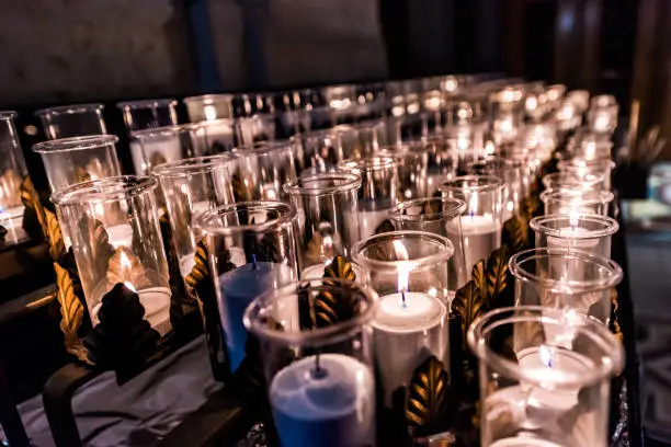 Closeup side pattern of many white religious votive candles with yellow flame in church or cathedral