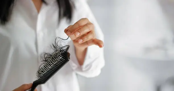 Photo of woman losing hair on hairbrush in hand on bathroom background