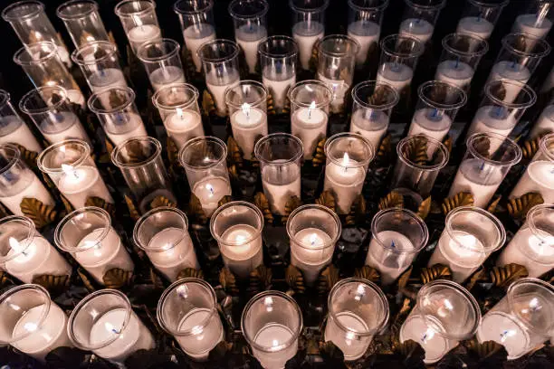 Closeup pattern of many white religious votive candles with yellow flame in church or cathedral