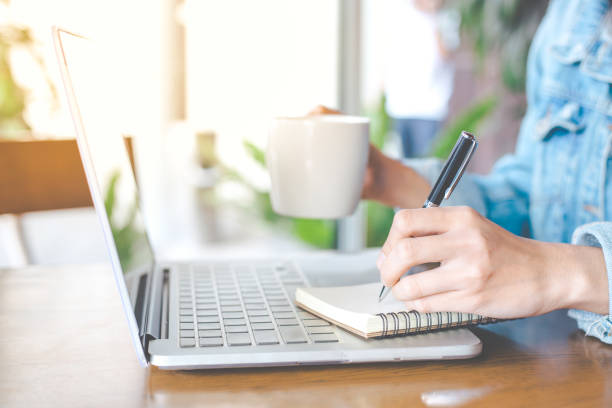 istock A woman's hand working on a notebook computer and writing on a notepad with a pen in the office. 846225278