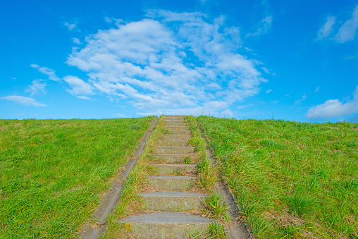 Green dike with a stairway below a blue cloudy sky