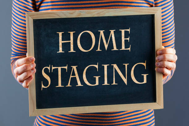 Female hands holding small black chalkboard in front of the body closeup with words Home Staging. On gray background with copy space stock photo