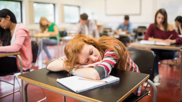 Blurred students in the classroom with one asleep girl Blurred young college students sitting in the classroom with one asleep girl male college student sleeping through lecture stock pictures, royalty-free photos & images
