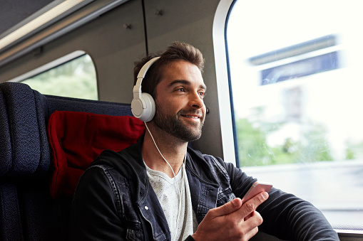 Dude on the move on train with tunes, smiling