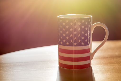 A flag of the United States of America on a mug close up with sun rays and blurry background