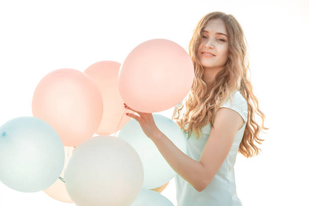 portrait of young beautiful woman with flying multicolored balloons against the sky.  soft light