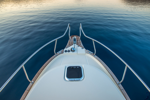 Bow of a luxury yacht with an anchor and a guard rail while moving on the blue sea