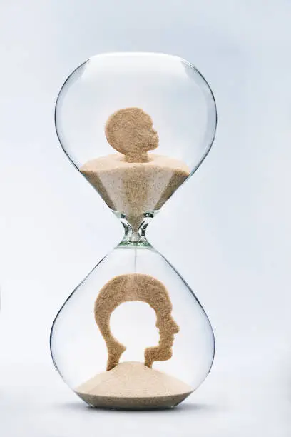 Childhood nostalgia concept with falling sand taking the shape of a cut out child head inside a man head, inside a hourglass