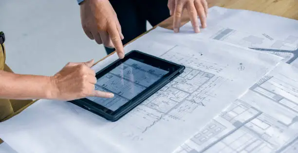 Male and female architect using digital tablet while discussing with construction plant at construction site.