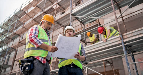 Male project superintendent discussing plans with foreman at construction site Male project superintendent and male foreman discussing plans at construction site wearing safety helmets. superintendent stock pictures, royalty-free photos & images