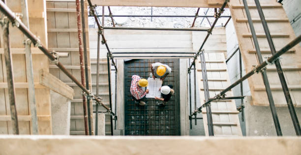 istock Female architect explaining details of plan to site manager and foreman standing at bottom of scaffold staircase 846307034