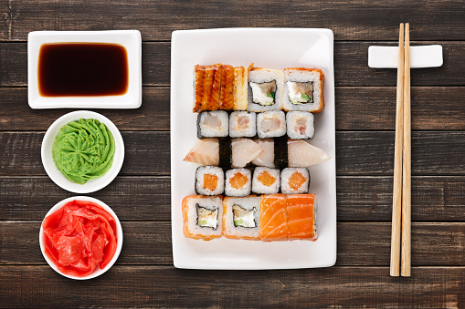 Japanese food restaurant delivery - sushi maki, unagi and roll platter set isolated on brown wood background, above view