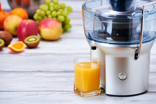Modern electric juicer, various fruit and glass of freshly made juice, healthy lifestyle detox concept