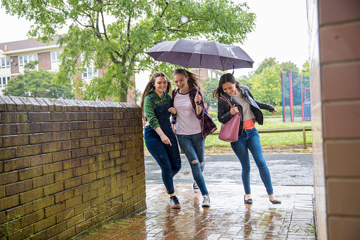 Three young women run for shelter in the rain while one holds an umbrella.