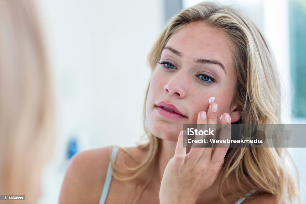 Smiling pretty woman applying cream on her face Smiling pretty woman applying cream on her face in bathroom Suntan Lotion Stock Photo