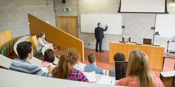 Rear view of a male teacher with students at the college lecture hall