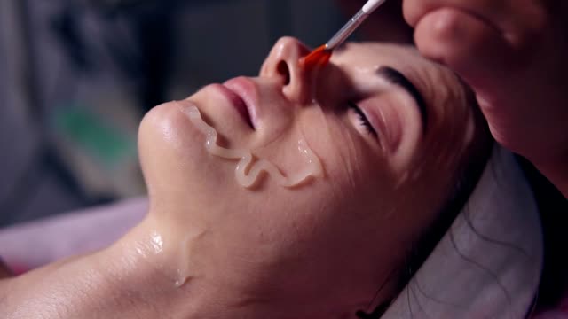 Professional carboxytherapy for young woman in spa salon. Young woman is lying on the couch while professional cosmetologist is apllying special treatment on woman's face using brush