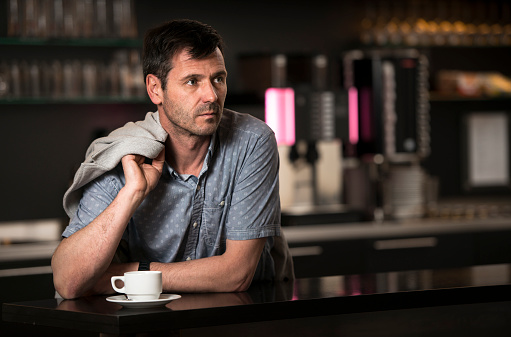 Handsome man leaning at the bar with a cup of coffee. He's looking serious and if his waiting for someone.