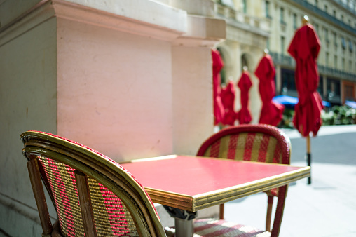 Typical table and rattan chairs on the terrace of a parisian outdoor cafe in the sunlight with parasols in the background.