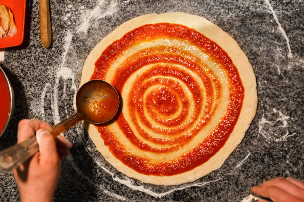 mano de la chef que se separa la pasta de tomate en la base de la pizza - makes the dough fotografías e imágenes de stock