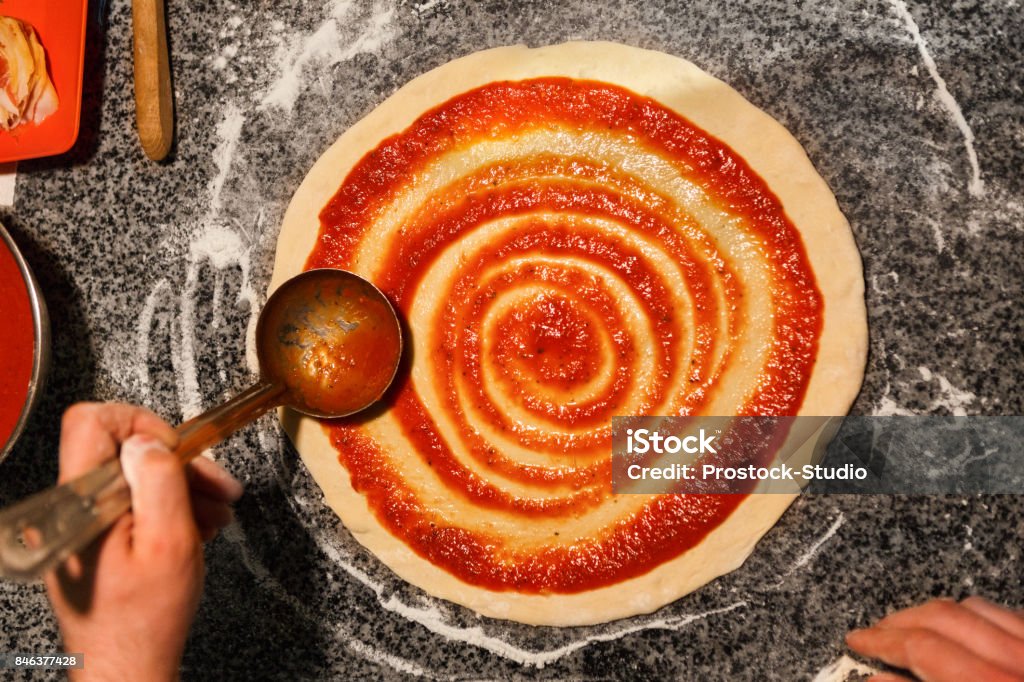 Chef hand spreading tomato paste on pizza base Chef hand spreading tomato paste on pizza base, preparing traditional italian meal with marinara sauce, copy space, top view Pizza Stock Photo