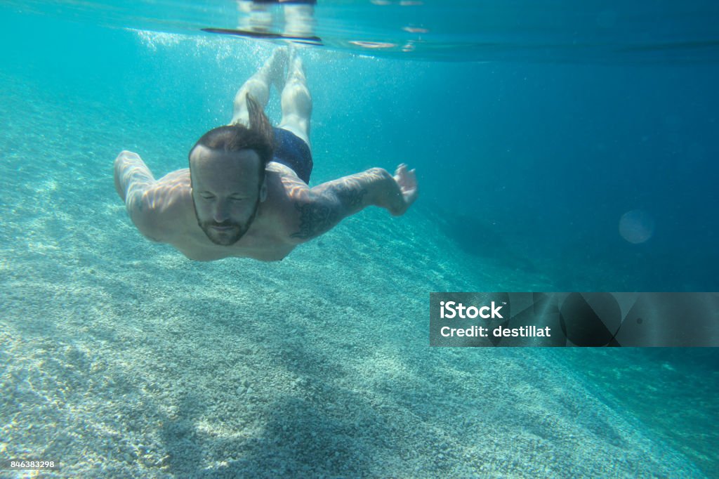 Man swimming underwater Man swimming underwater in blue transparent sea water Males Stock Photo