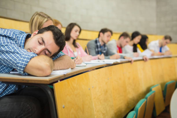Male sleeping with students in lecture hall Male sleeping with students sitting in the college lecture hall male college student sleeping through lecture stock pictures, royalty-free photos & images