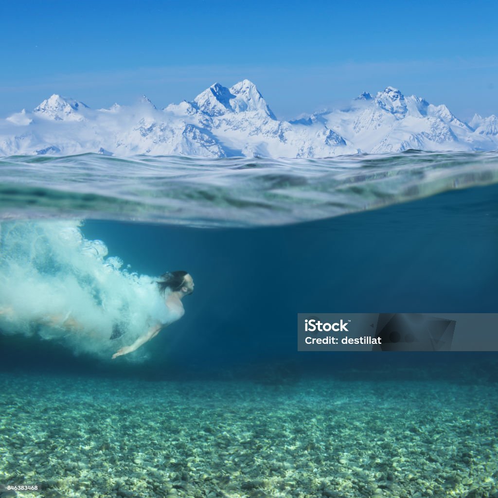 Man swimming underwater Man swimming underwater in blue transparent sea water, snow mountains on background Swimming Stock Photo